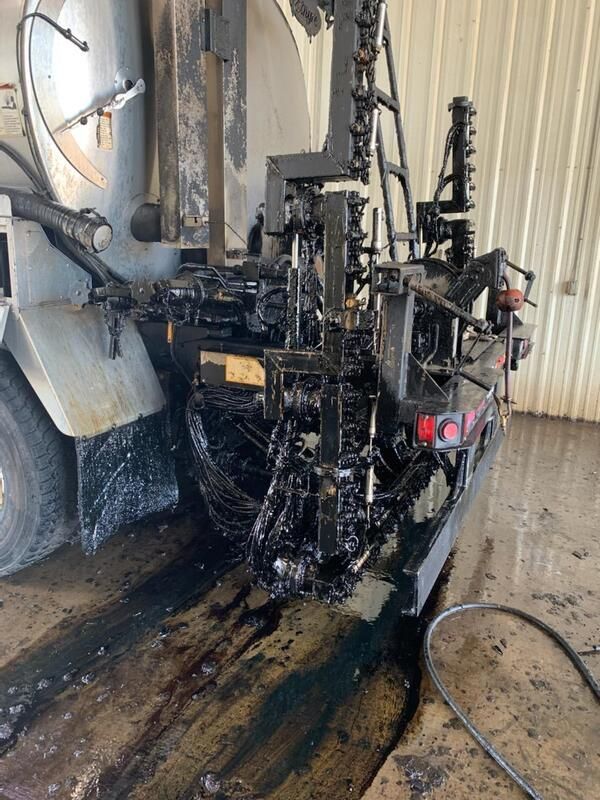 Charred machine mounted on a truck, with black soot and spilled liquid staining the ground in an industrial area