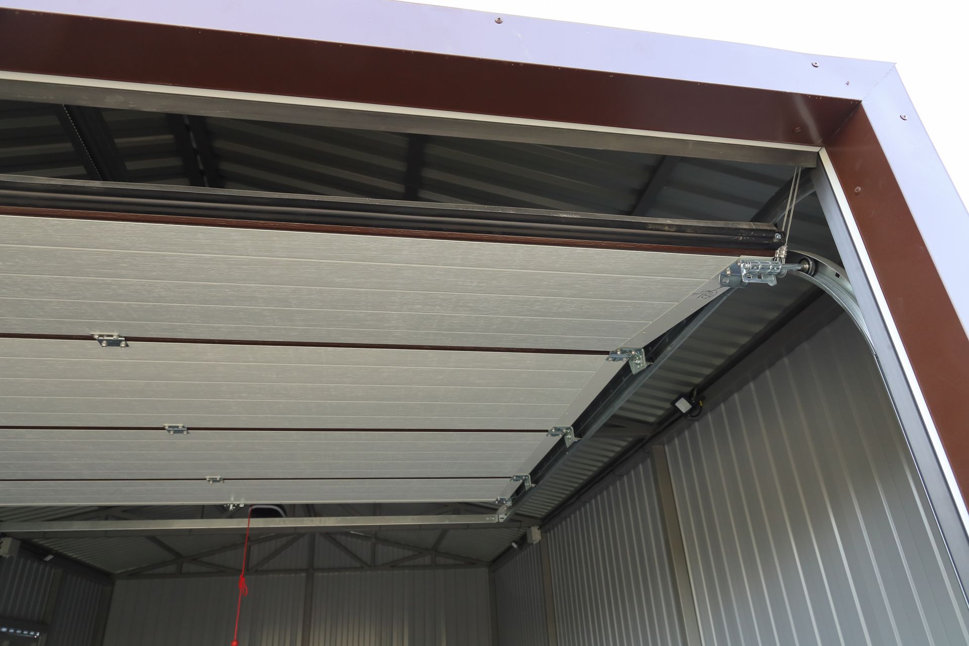 Insulated sectional garage door with metal framing inside steel shed, showing ceiling tracks system.