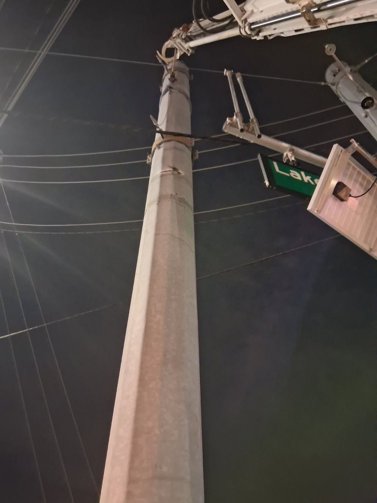 Utility pole with power lines at night and a bucket truck lift near a street sign