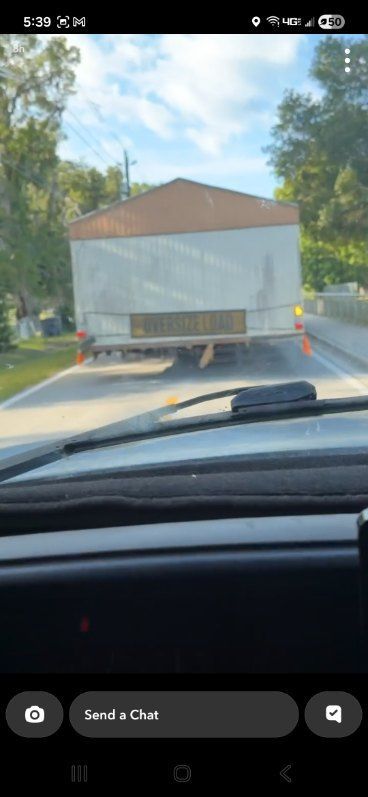 View through a car windshield of a large white truck driving on a tree-lined road.