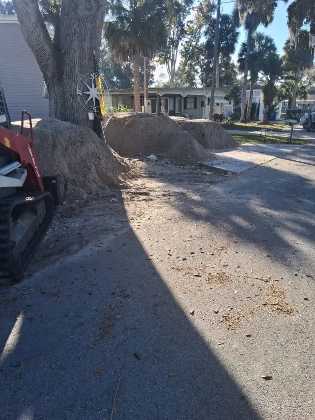 A red skid steer parked next to large mounds of dirt on a paved residential street in front of a house.