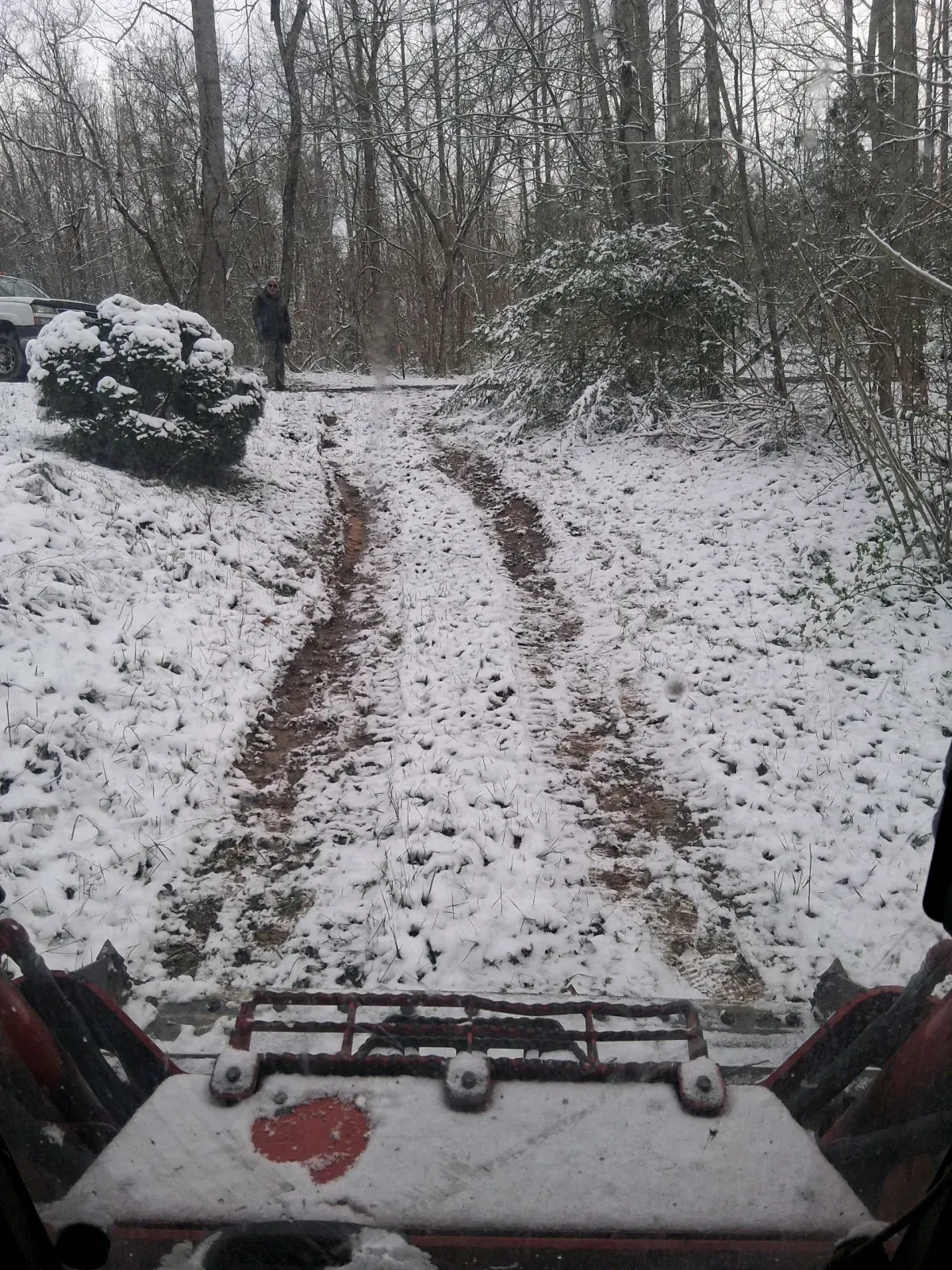 A view from the driver's seat of a vehicle looking out over a snow-covered path into a wooded area.