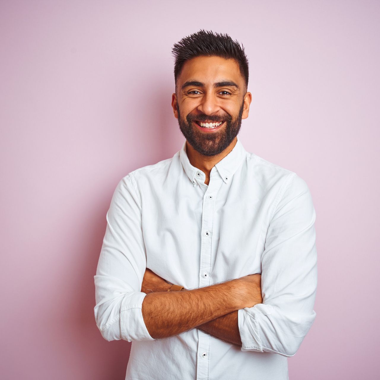 A man with a beard is standing with his arms crossed and smiling.