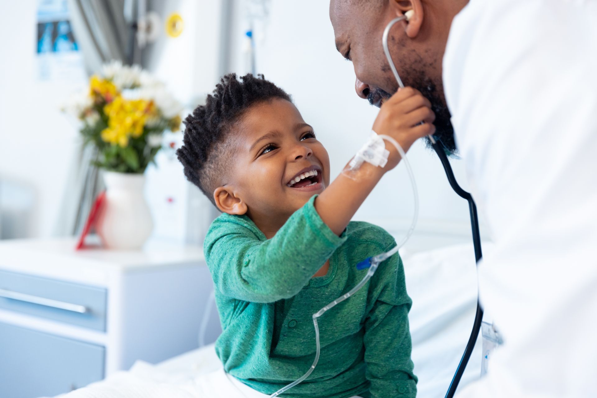 A little boy is playing with a stethoscope on a doctor 's ear in a hospital room.