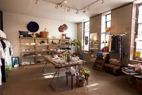 Interior of a retail store with clothing, accessories, and a display table. Shelves line the wall.
