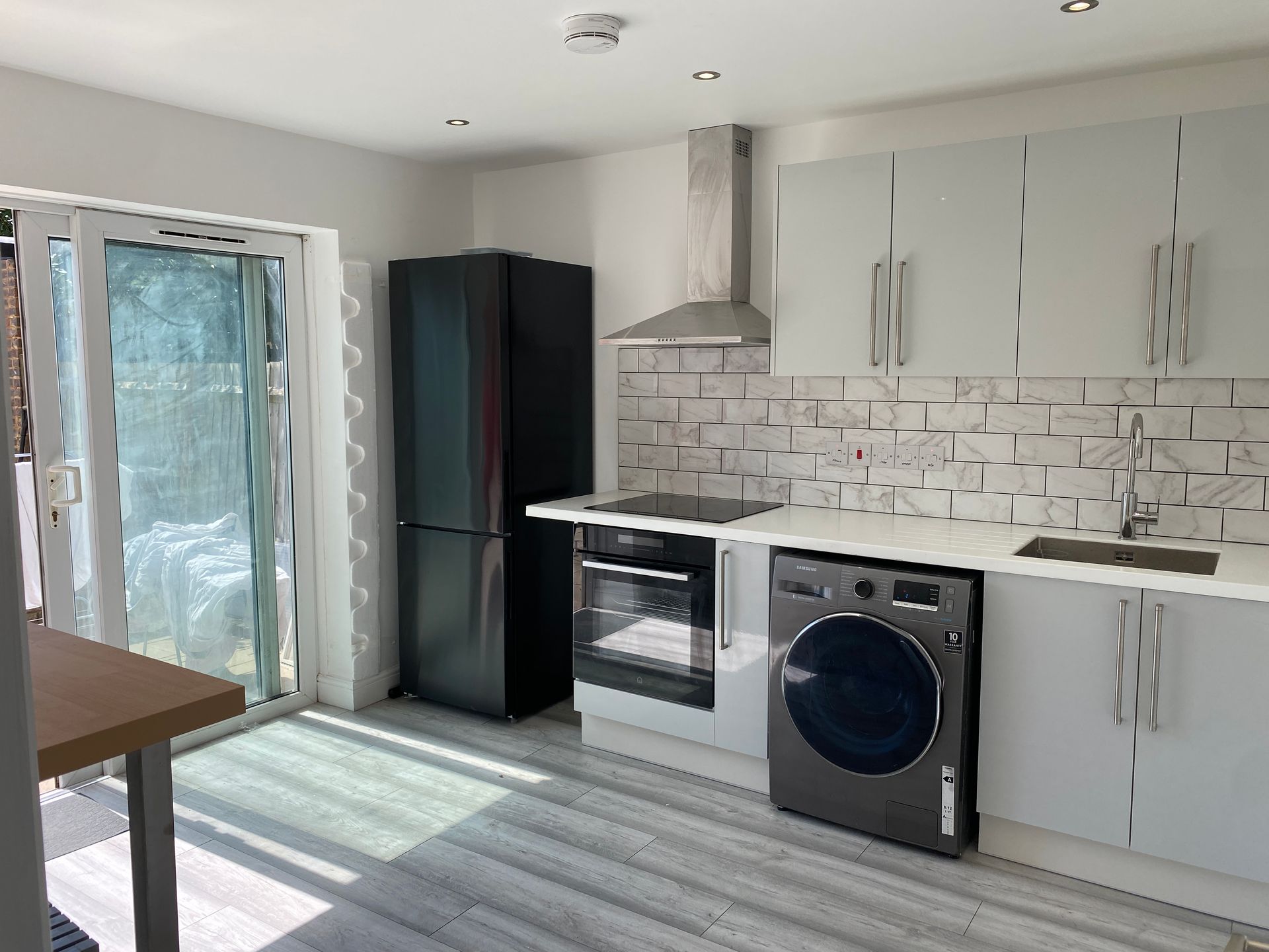 A kitchen with a refrigerator , washing machine , oven , sink and sliding glass doors.