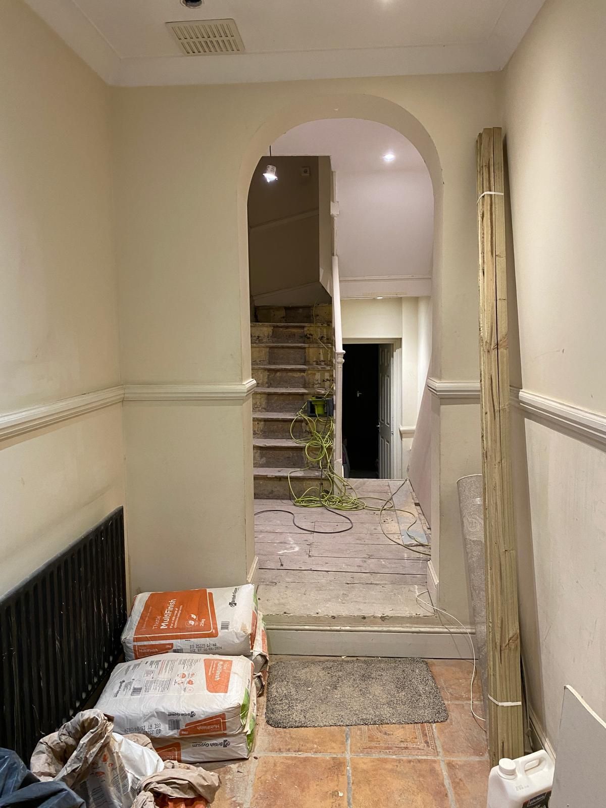 A hallway with a staircase in the background and bags of cement on the floor.