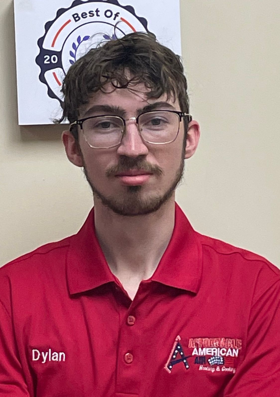 A young man wearing glasses and a red shirt is standing in front of a sign that says best of.