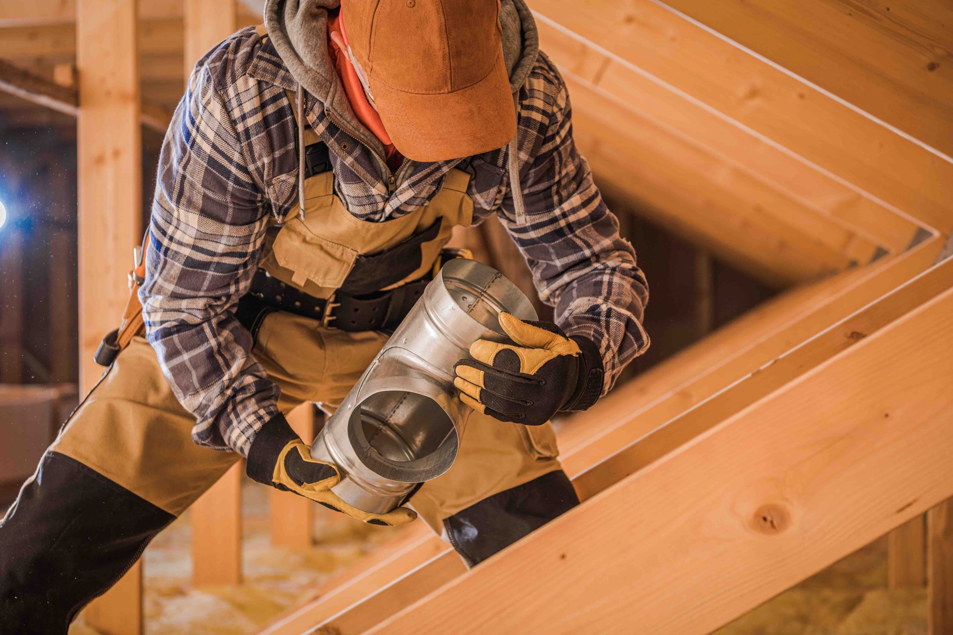 A man is working on a pipe in an attic.