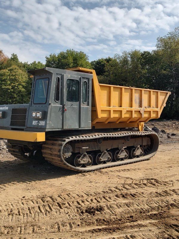 A dump truck is parked next to a small excavator in a yard.