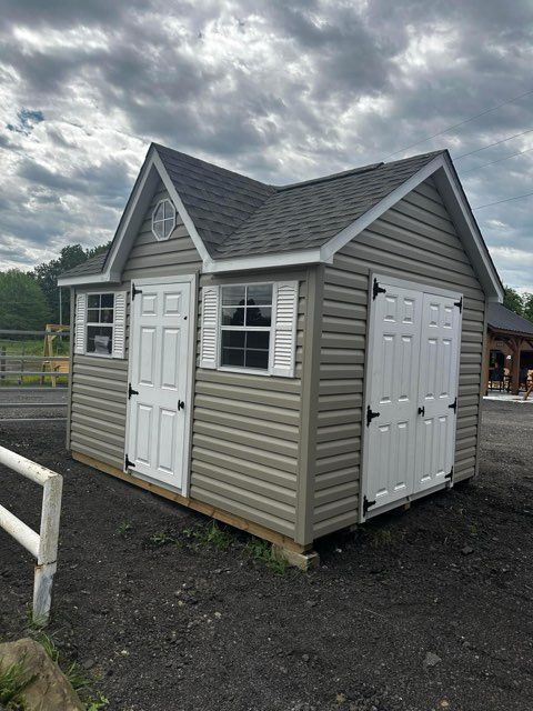 A small shed with a roof and shutters is sitting on top of a dirt field.