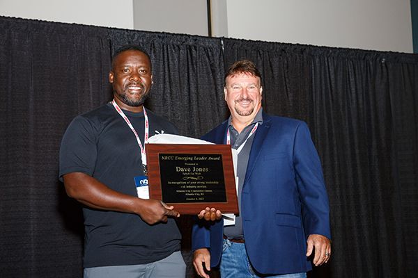Two men holding a plaque at an awards ceremony, standing in front of black curtains.