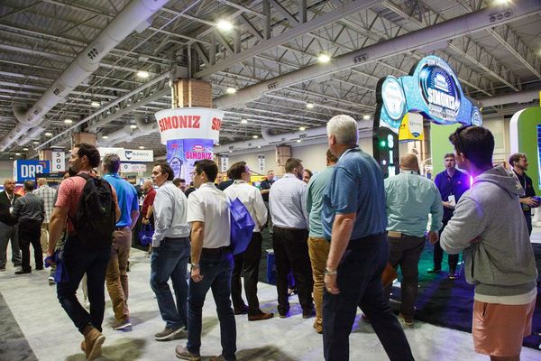 Crowd of people browsing booths at a brightly lit indoor trade show or expo.
