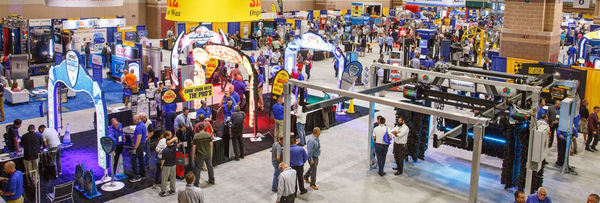 Crowded trade show floor with colorful booths, displays, and many people walking around