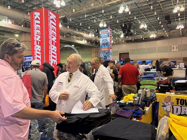Trade show booth with people chatting near KEEPER-branded banners and display tables.