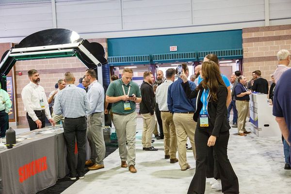 People mingling at a trade show booth with a large display and table in an indoor convention hall