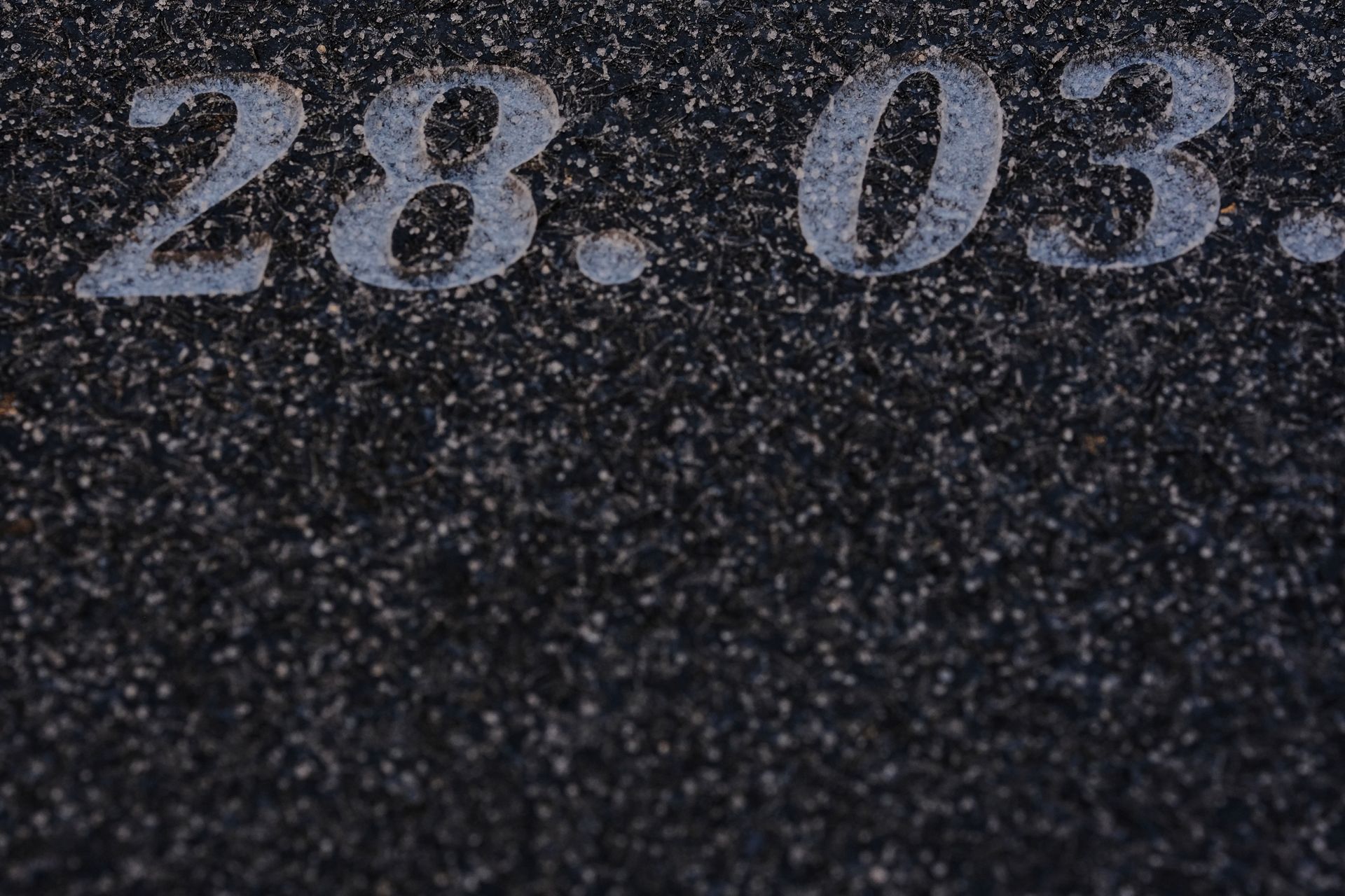 Laser-etched date numerals on a polished black granite monument close-up.