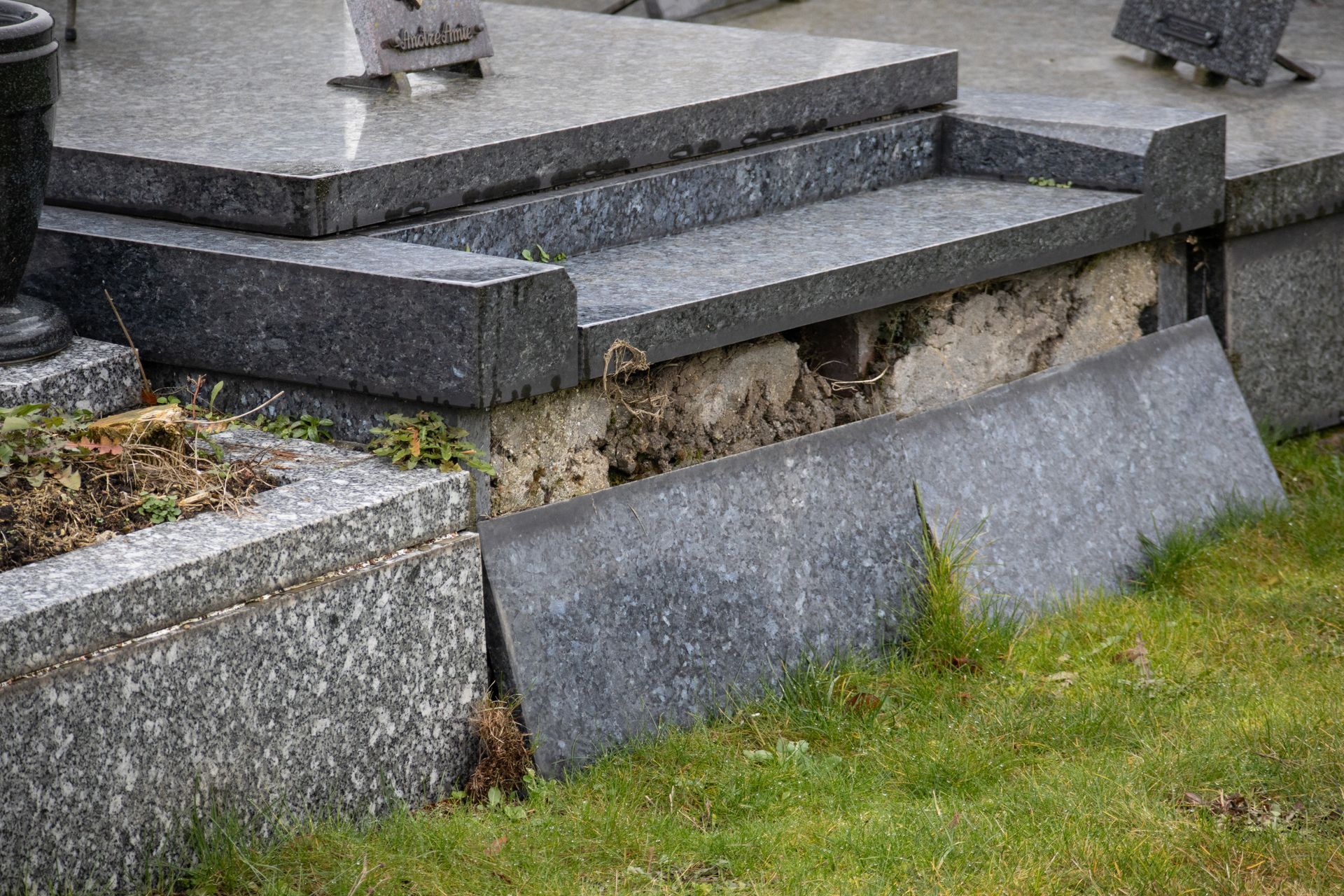 Damaged granite tombstone in a cemetery with a broken stone slab.