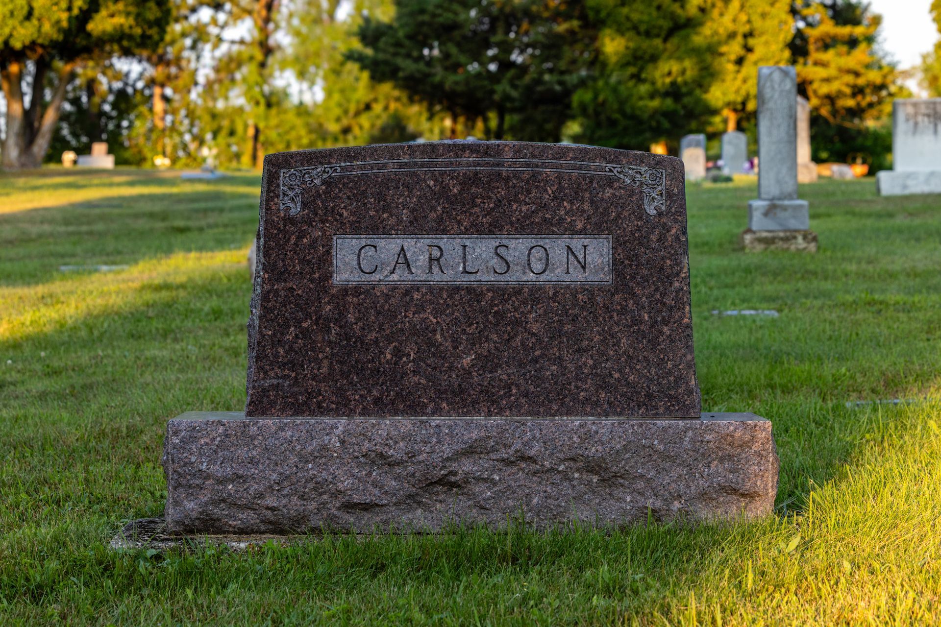 Upright brown granite grave monument engraved CARLSON in a sunlit cemetery.