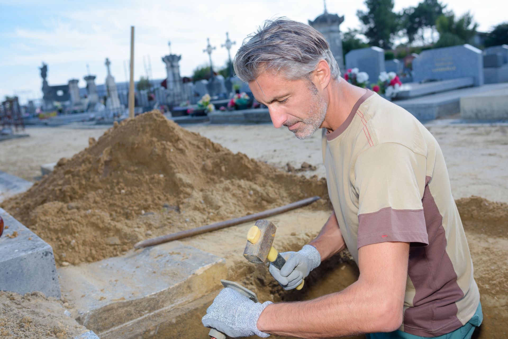 A man carefully constructing a grave in a serene cemetery, surrounded by trees and headstones.