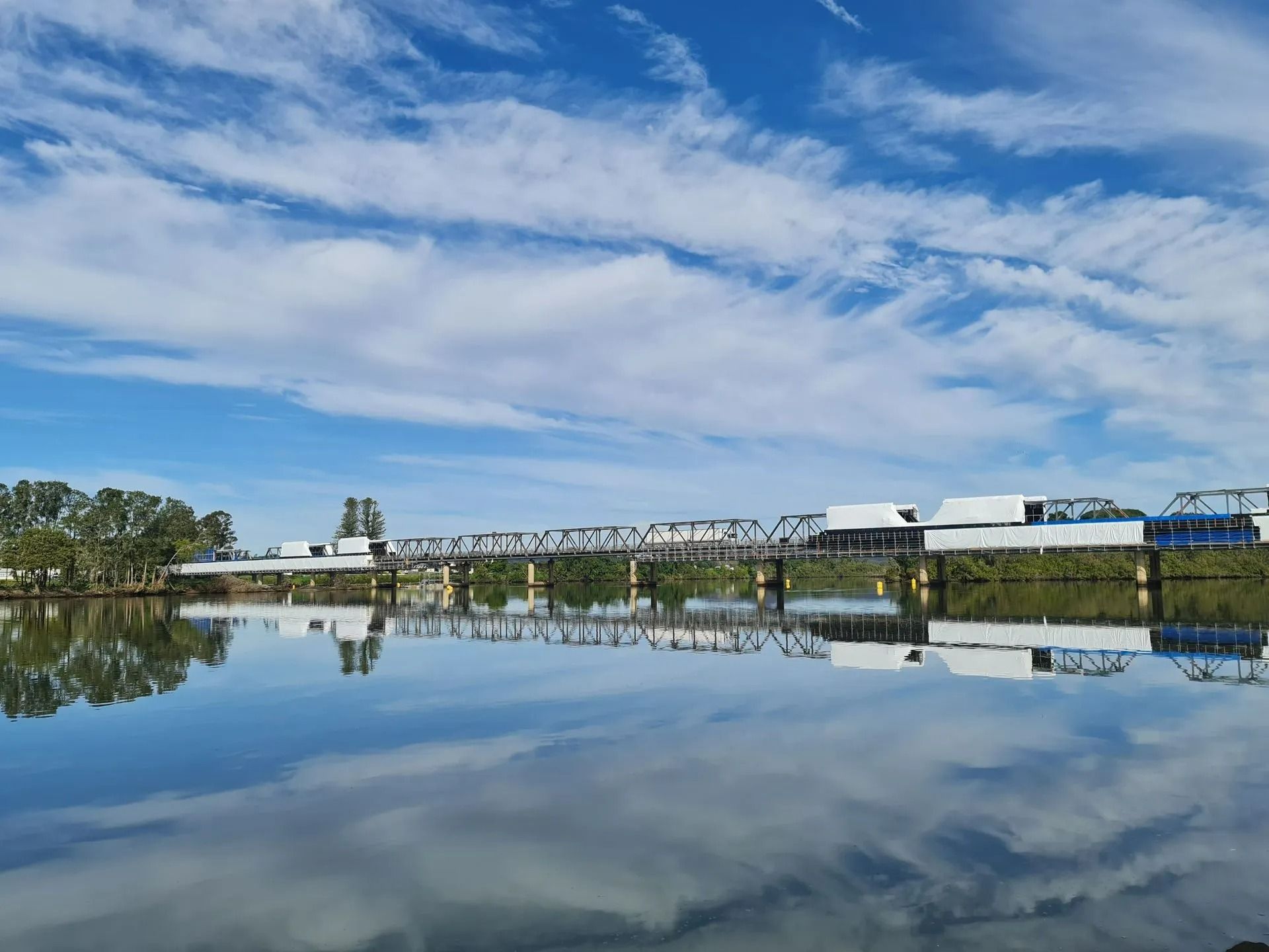 A Bridge Over a River with A Blue Sky and Clouds Reflected in The Water — Oz-Craft in Taree, NSW