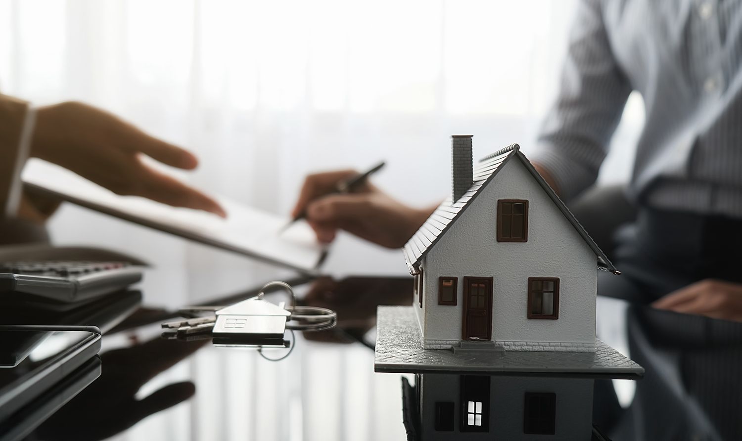 Small house model on a desk with people signing papers