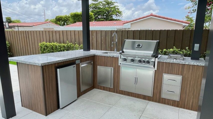 Outdoor patio kitchen with grill, mini fridge, countertop, and storage cabinets under a covered structure