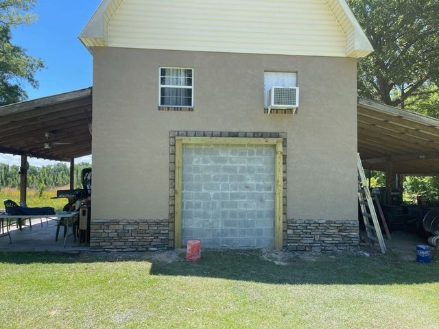 Small beige building with a closed cinderblock door, two windows, and covered side patios on grass.