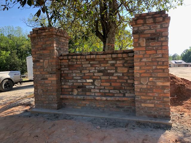 Brick wall under construction with two brick pillars and a central low wall on a dirt lot