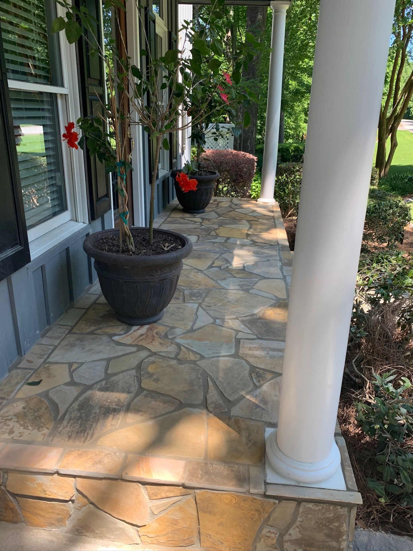 Stone front porch with white columns, potted plants, and a windowed exterior wall