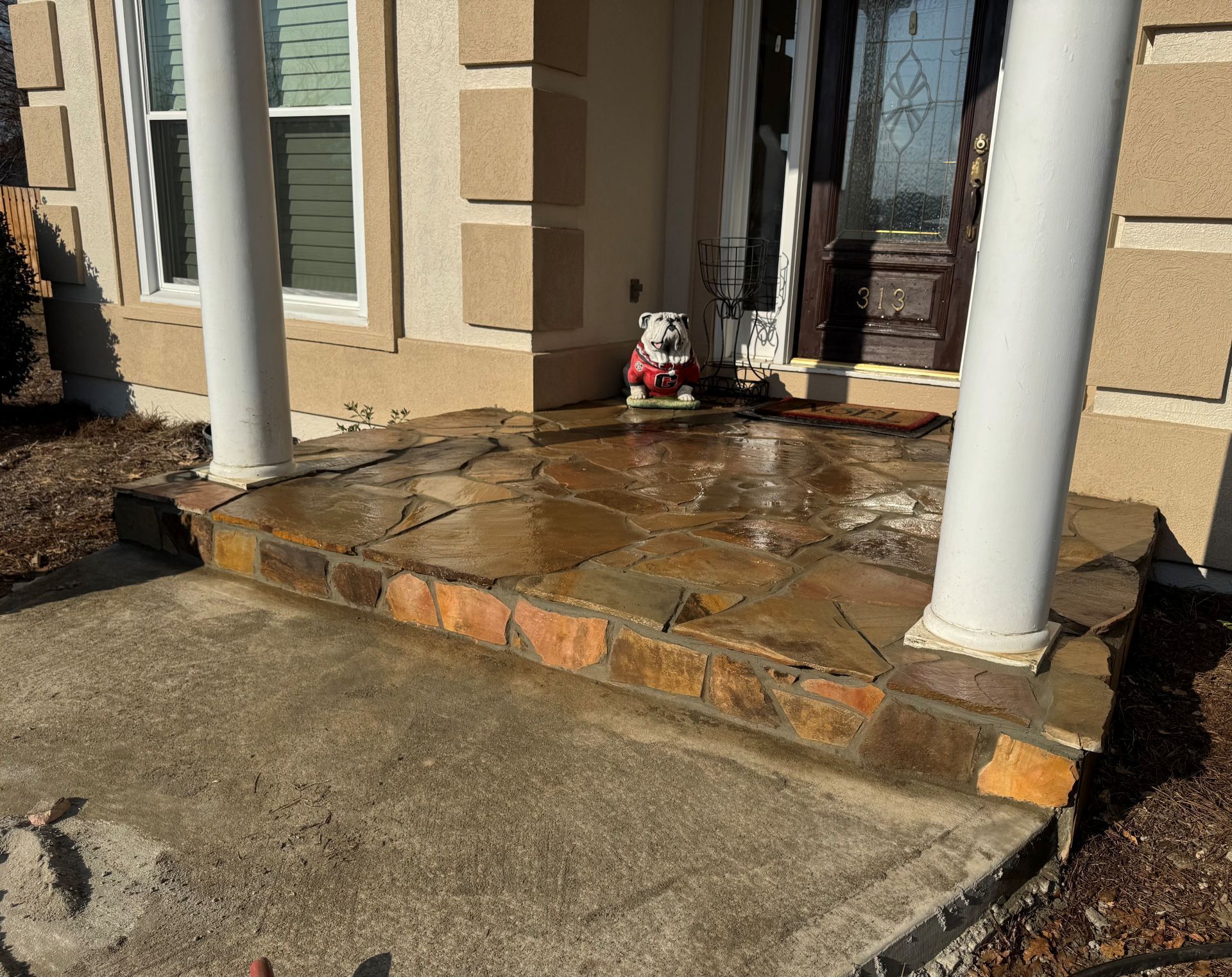 Front porch with two white columns, wet stone steps, and a small holiday decoration by the door