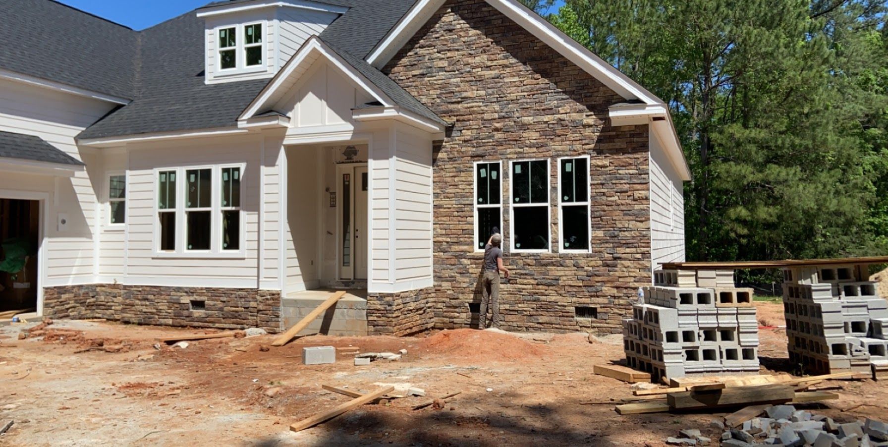 New house exterior under construction with brick and siding, white shutters, and stacked pallets in front