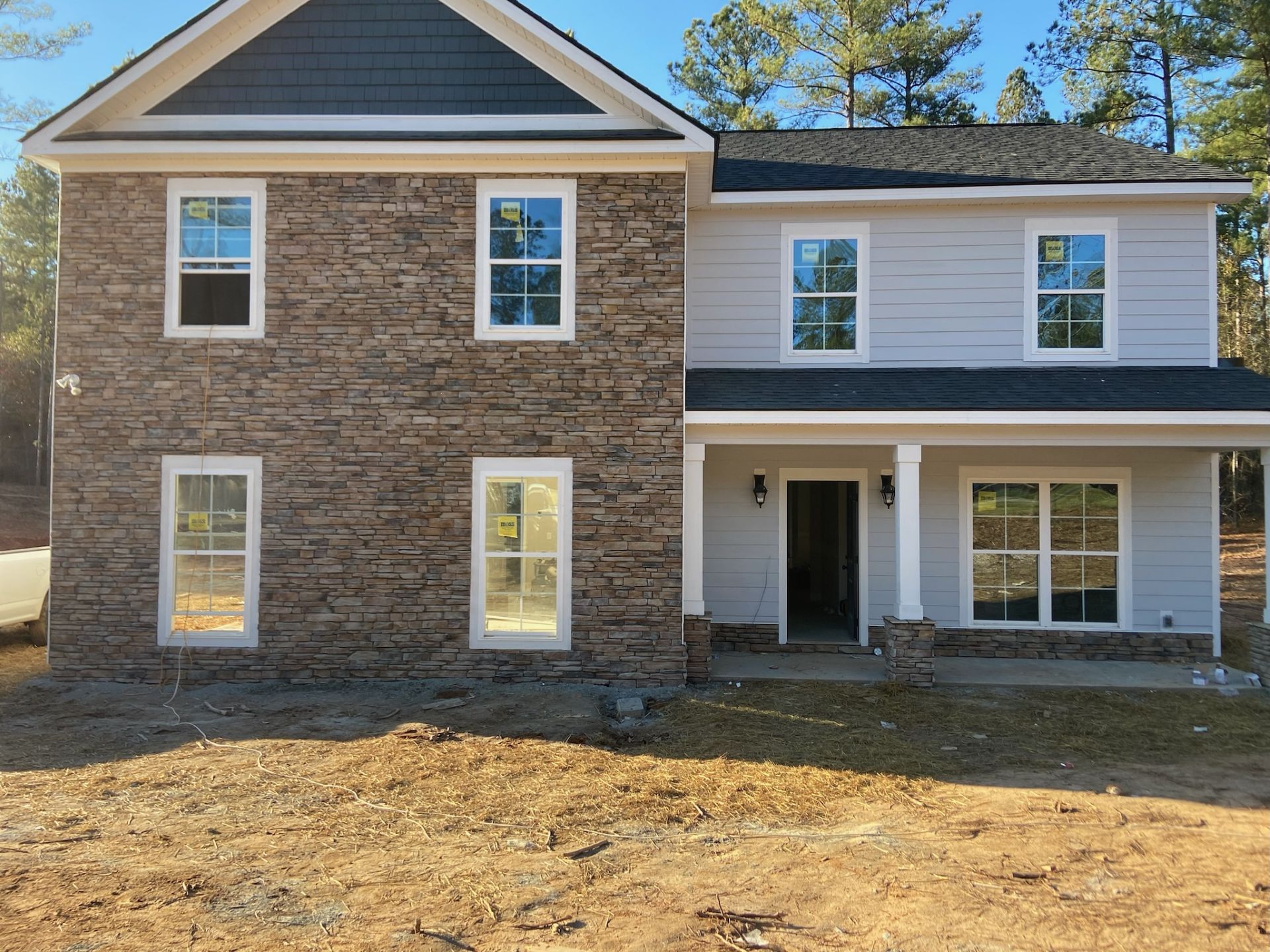 Two-story house exterior with stone and white siding, front porch, and unfinished dirt yard
