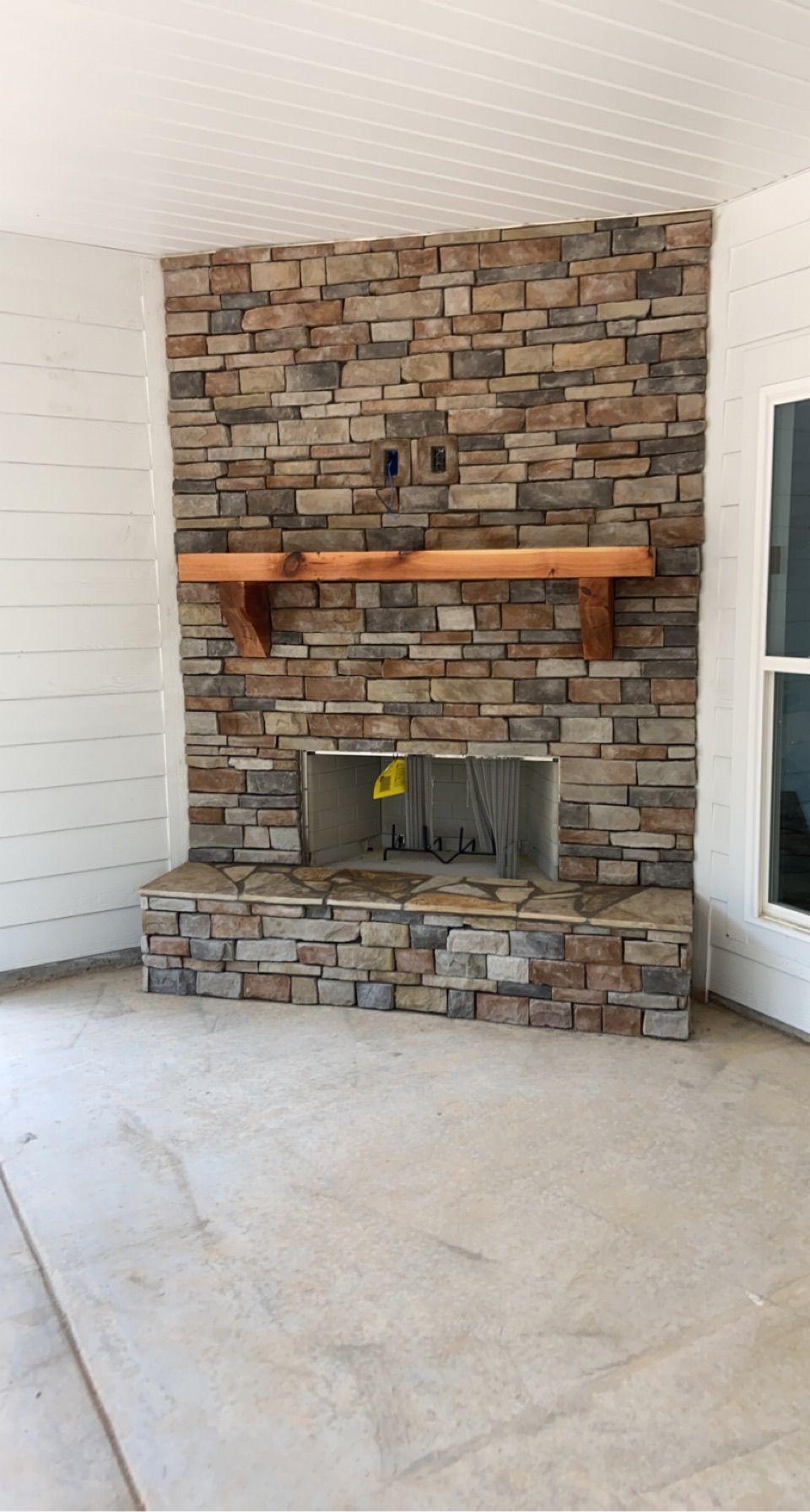 Stone fireplace with wooden mantel in a light-colored room, set against a white paneled wall.