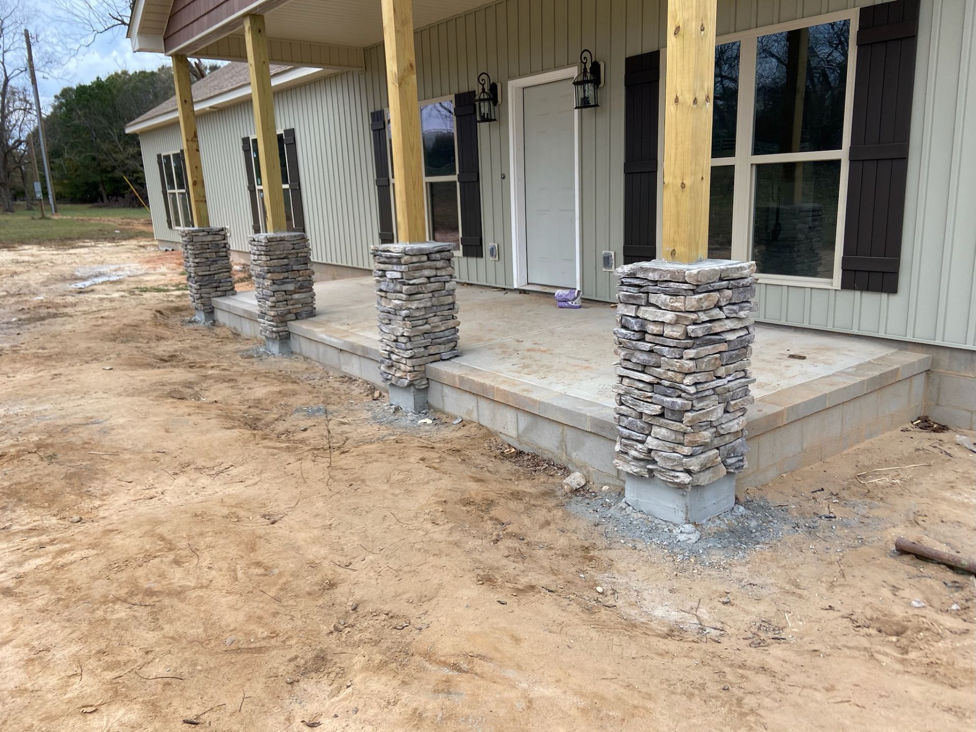 Front porch with stone columns and a white door on a house under construction