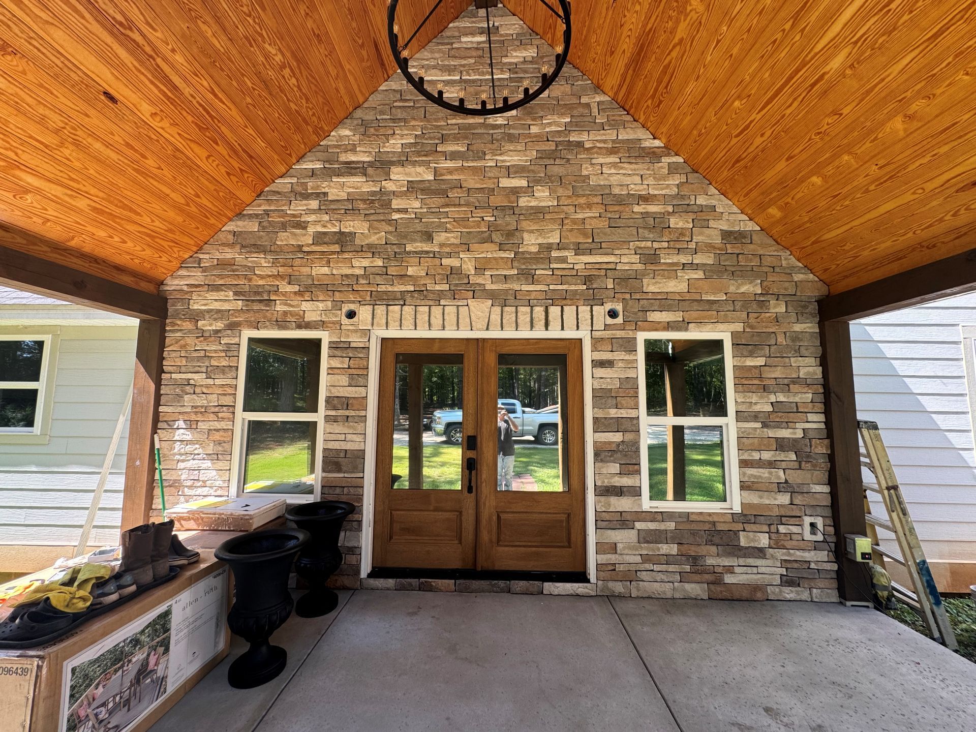 Covered stone porch with wooden double doors, windows, and a vaulted wood ceiling.