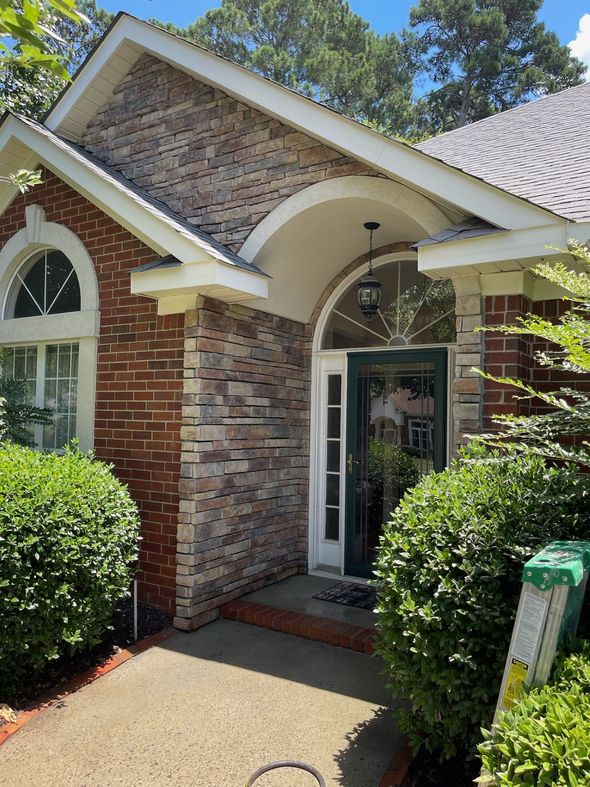 Brick townhouse entrance with white trim, arched doorway, and trimmed shrubs along the walkway