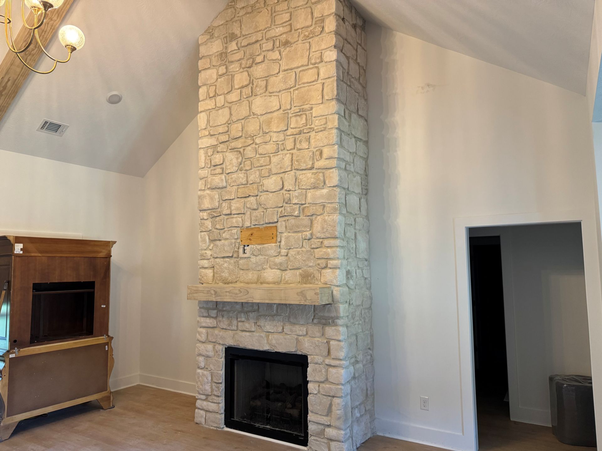 Living room with a tall stone fireplace, white walls, and a small wooden cabinet