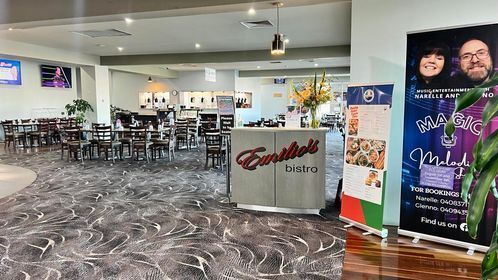 Empty restaurant dining area with tables, gray patterned floor, and colorful posters near the entrance