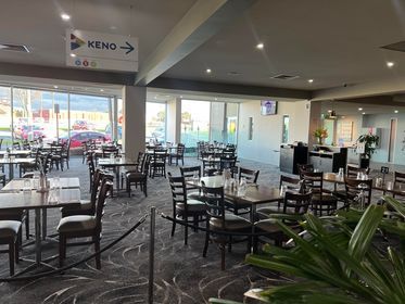 Empty restaurant dining area with tables and chairs, large windows, and a “KENO” sign overhead