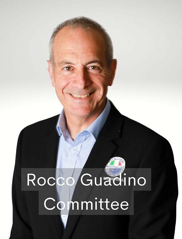 Portrait of Rocco Guadino in a dark blazer and blue shirt, smiling against a white background; Committee label visible