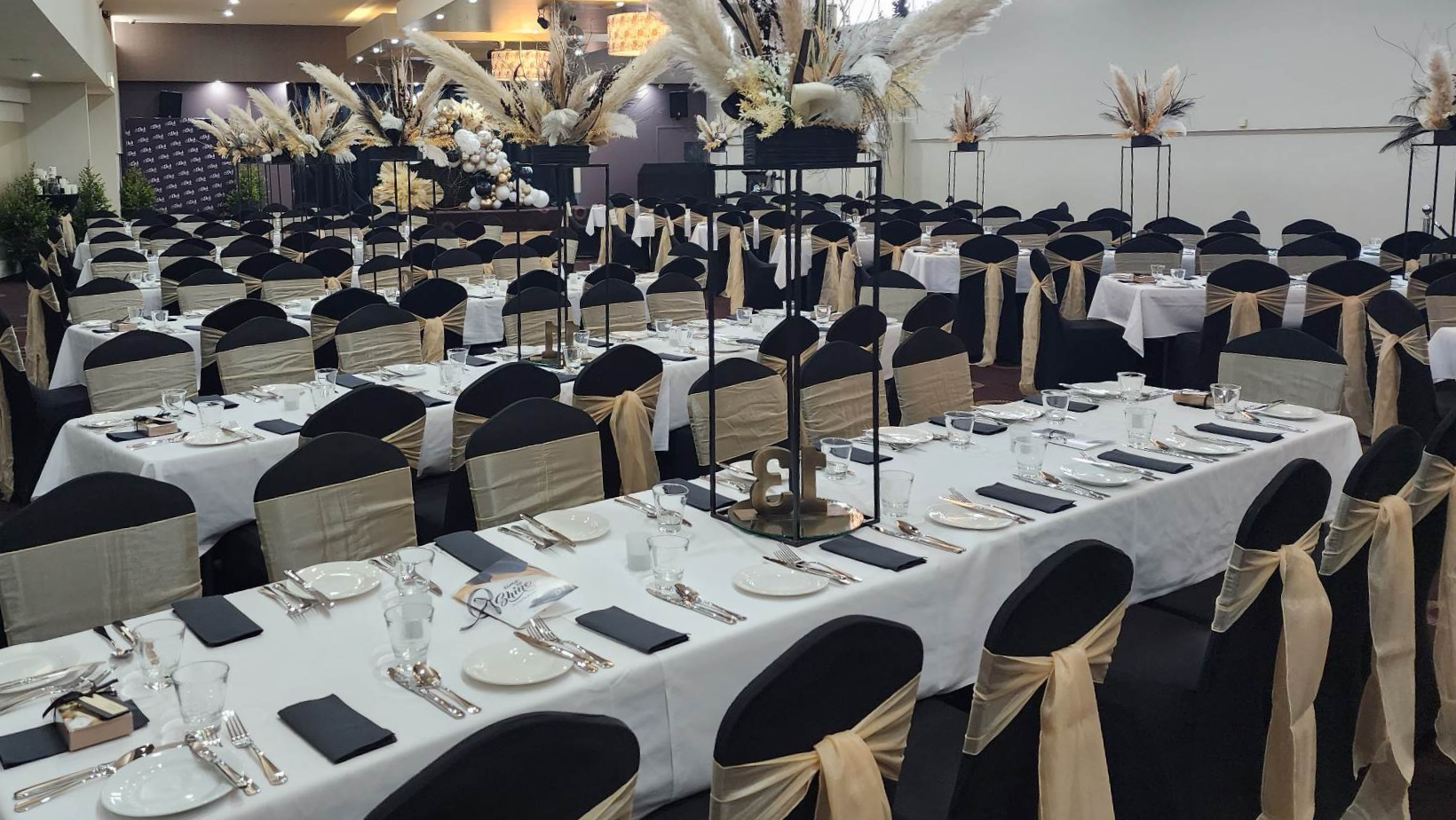 Elegant banquet hall with rows of white-clothed tables, black chairs, and floral centerpieces set for an event