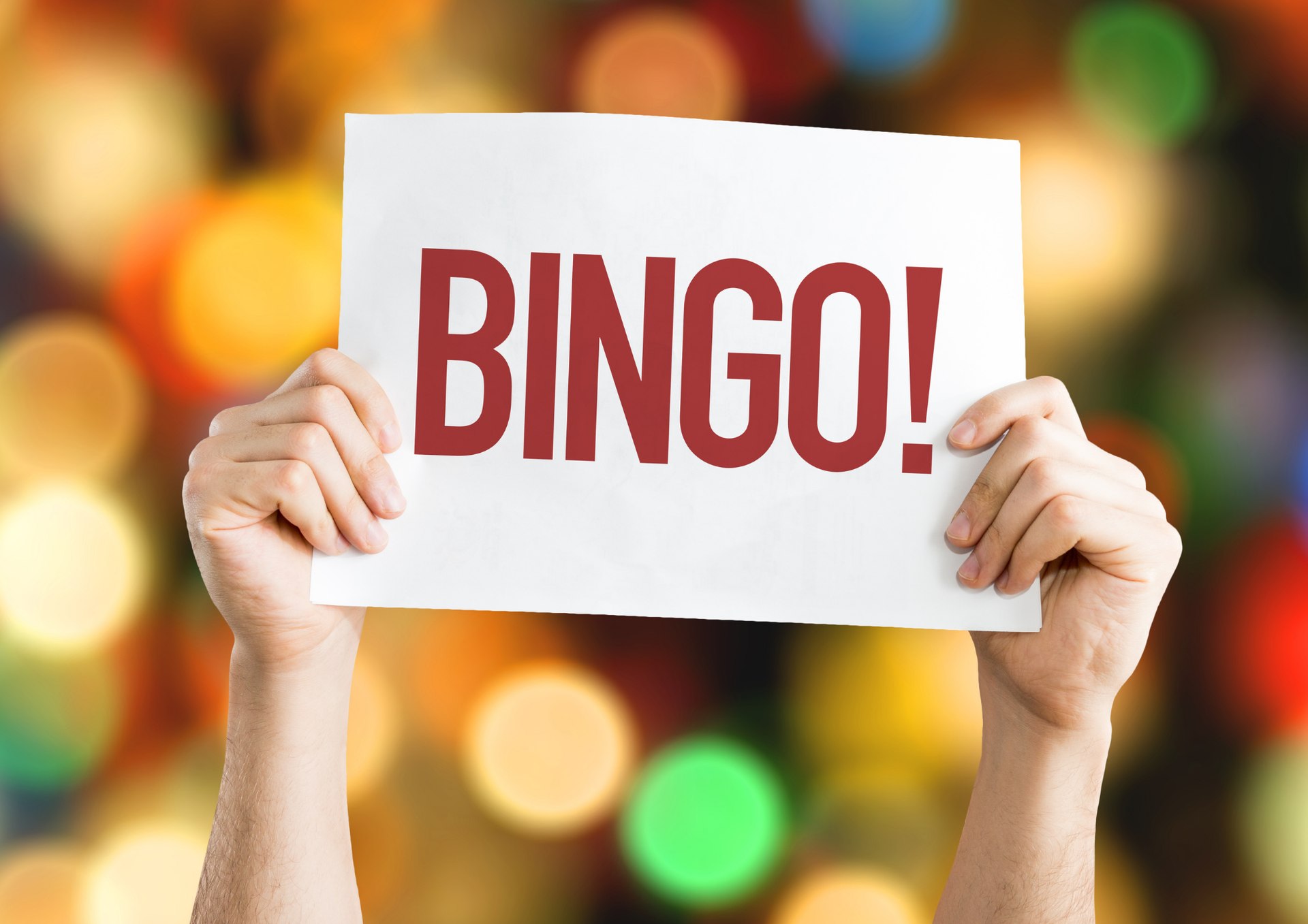 Hands holding a white sign that says “BINGO!” against a colorful blurred background