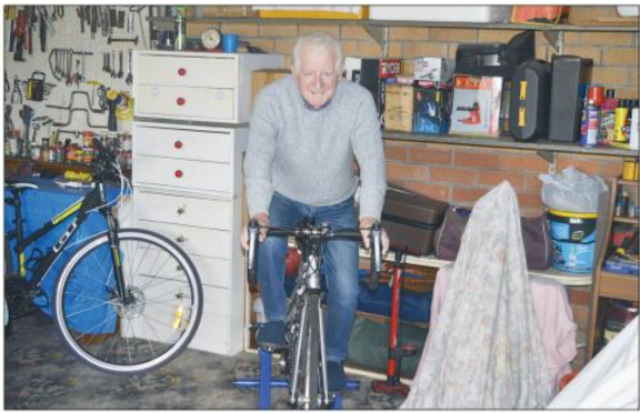 Man standing on a bicycle in a cluttered garage with tools, shelves, and a blue bike nearby