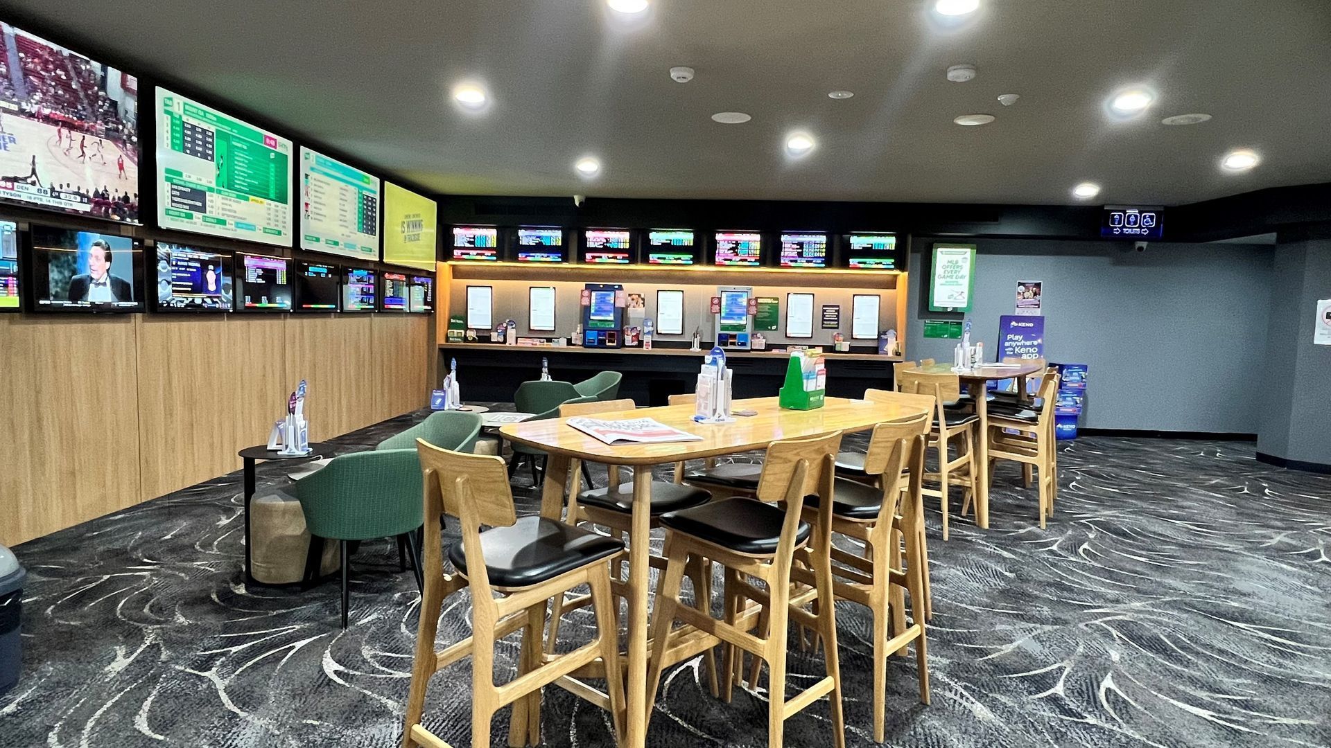 Sports bar with wall-mounted TVs, wood tables, and bar seating in a dimly lit room