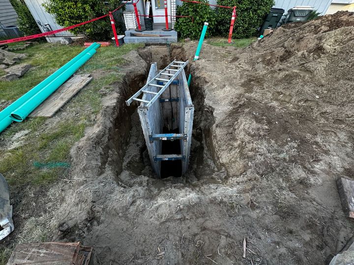 Construction trench with a metal box form, dirt piles, and green pipes beside it