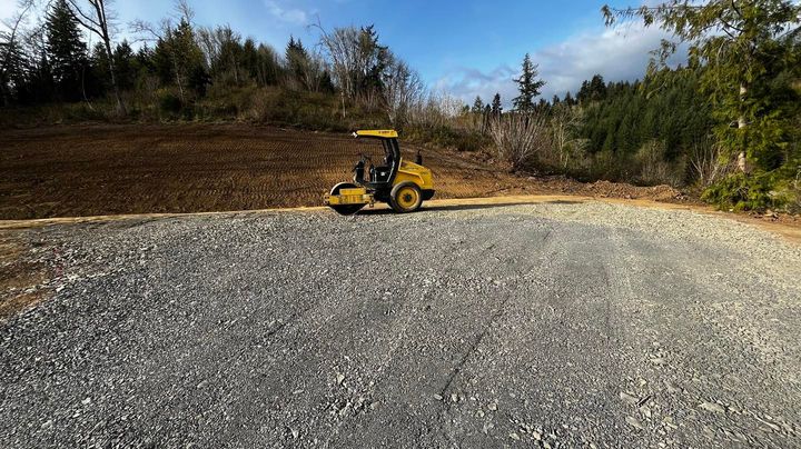 Yellow skid steer on a gravel lot with trees and blue sky in the background