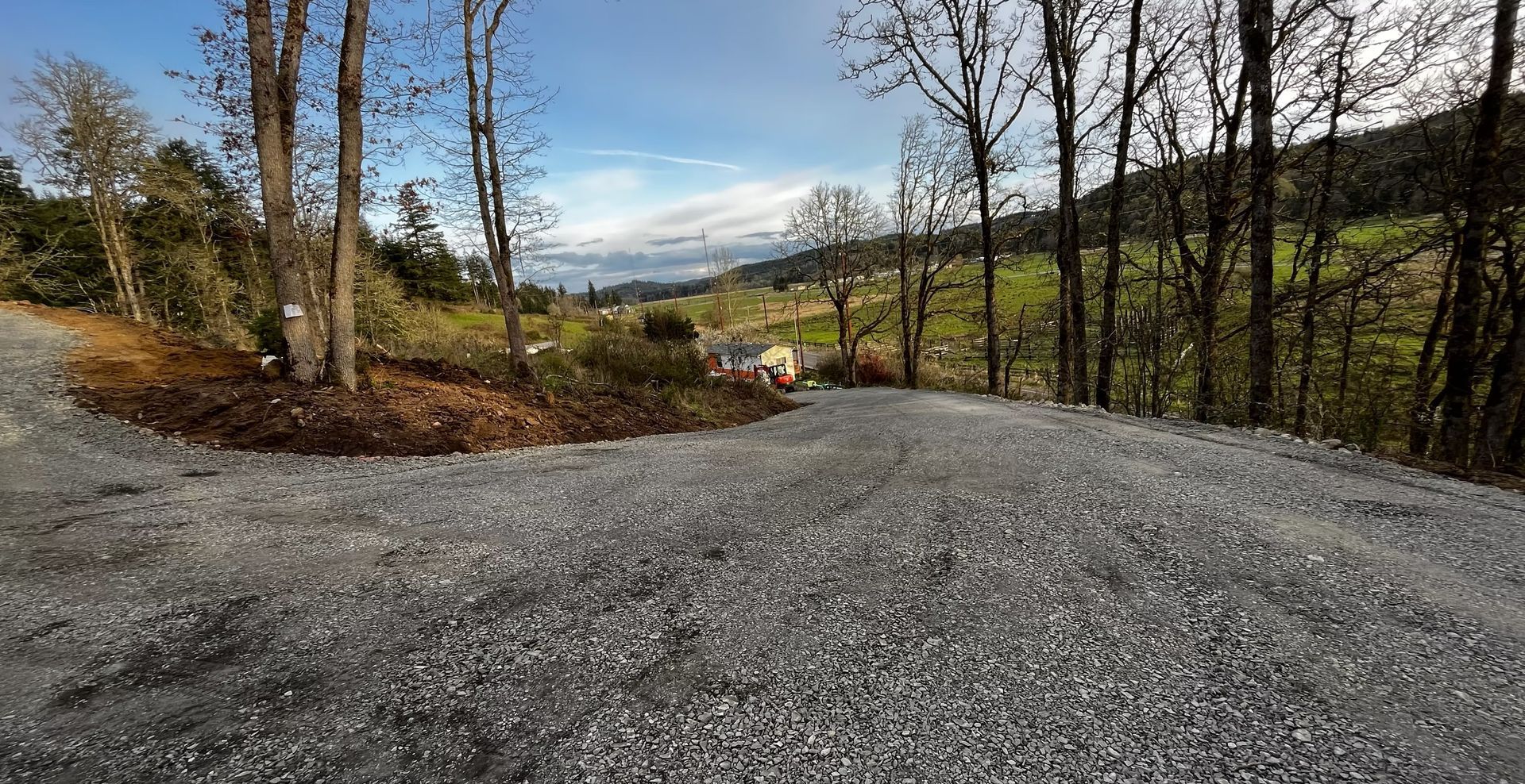 Gravel road curving through leafless trees with hills and valley in the distance
