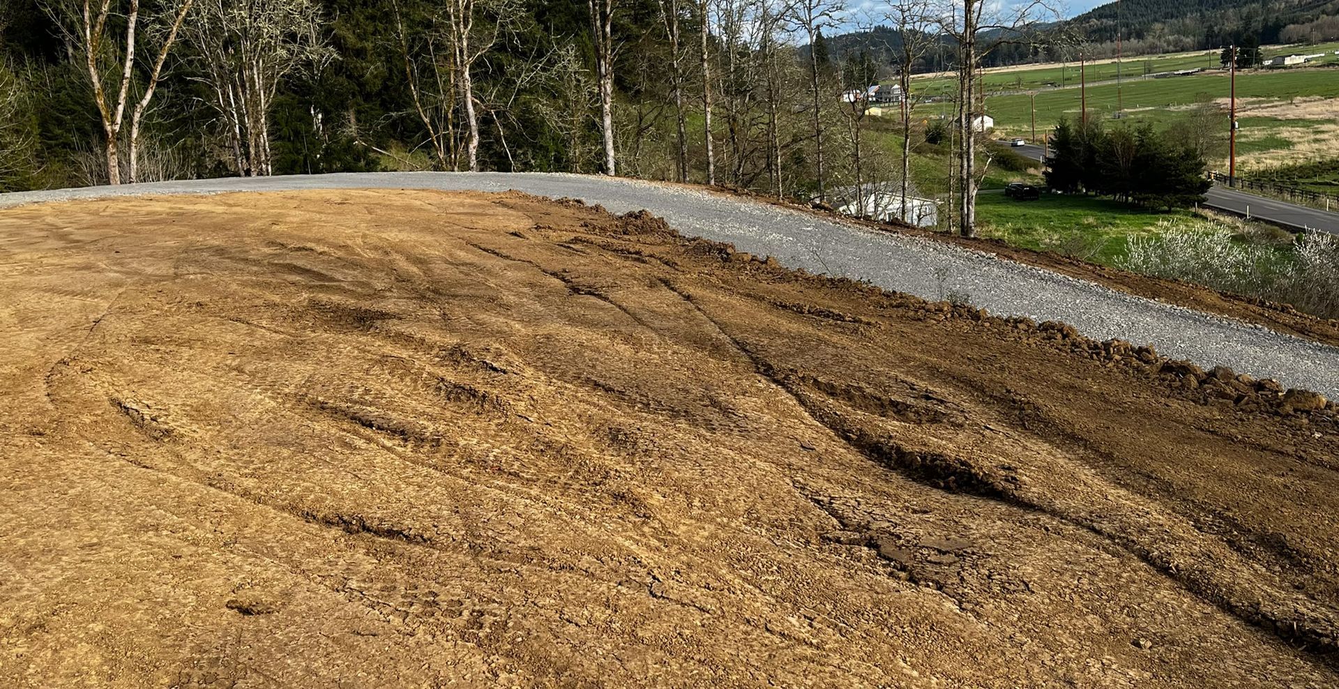 Freshly graded dirt embankment beside a gravel path, with trees and fields in the background