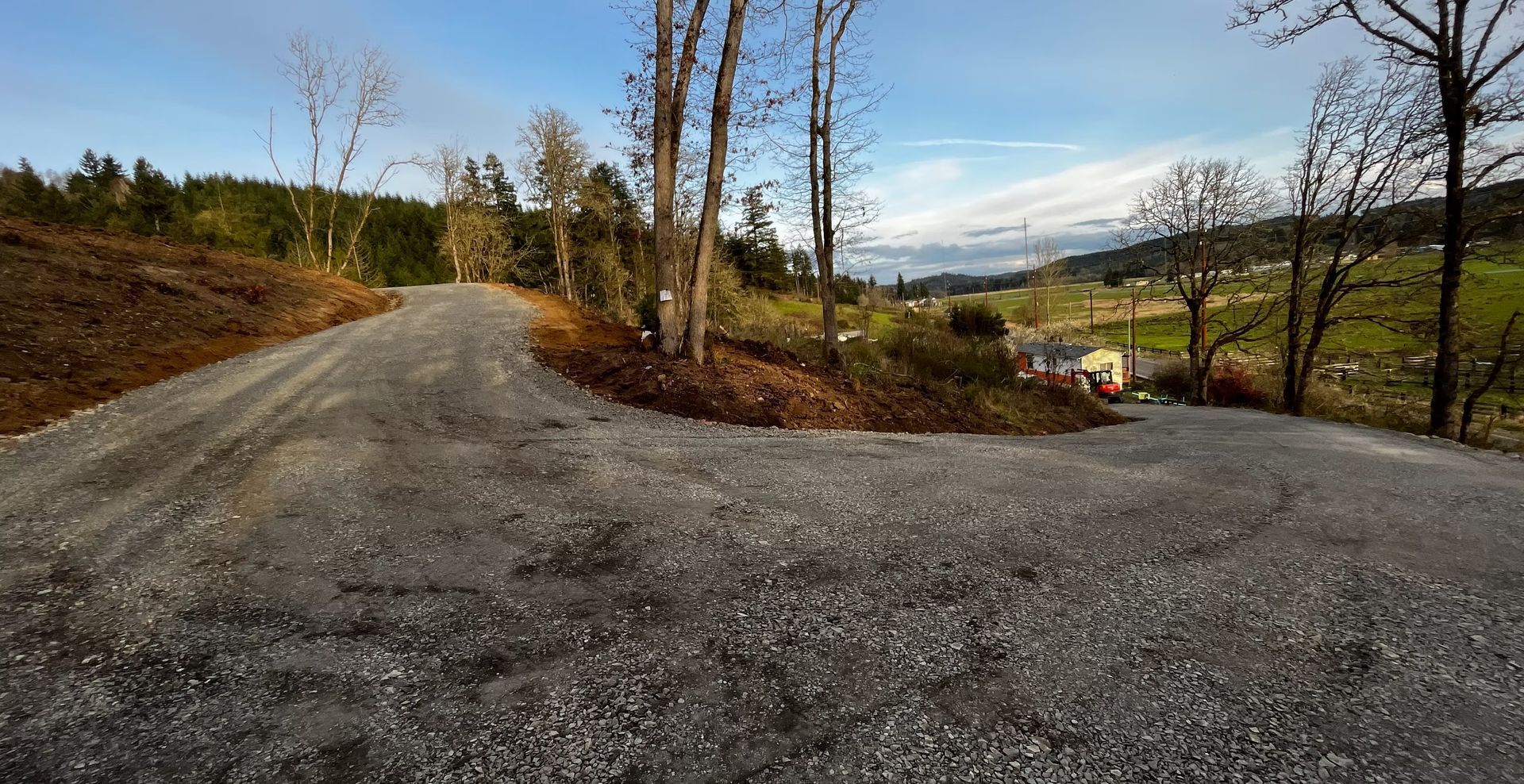 Gravel road fork in a rural hillside landscape with bare trees and a cloudy sky